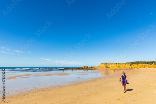 Female tourist walking along sandy coastal beach in summer photo