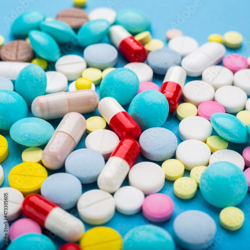 A lot of multi-colored pills on blue background with free space for text, as a concept of medical treatment with a prescription. Painkillers and antibiotics variation, allergy on medicine.