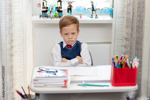 Cute boy first grader in school uniform at home during a break fooling around while sitting at his desk. Selective focus. Close-up. Portrait