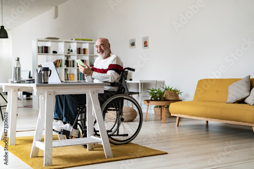 Senior disabled businessman with mobile phone and laptop at home office photo