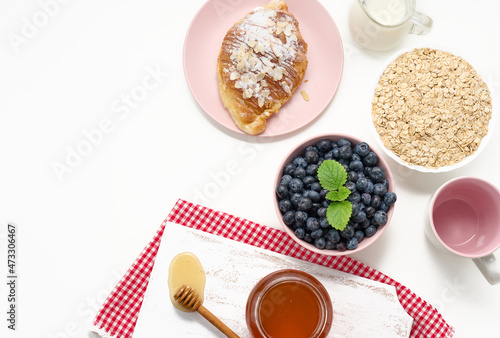 Raw oatmeal in white ceramic plate, blueberry, honey on white table, breakfast. top view