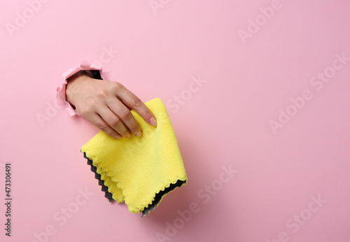 female hand sticking out of a torn hole in a pink paper background and holding a dry rag
