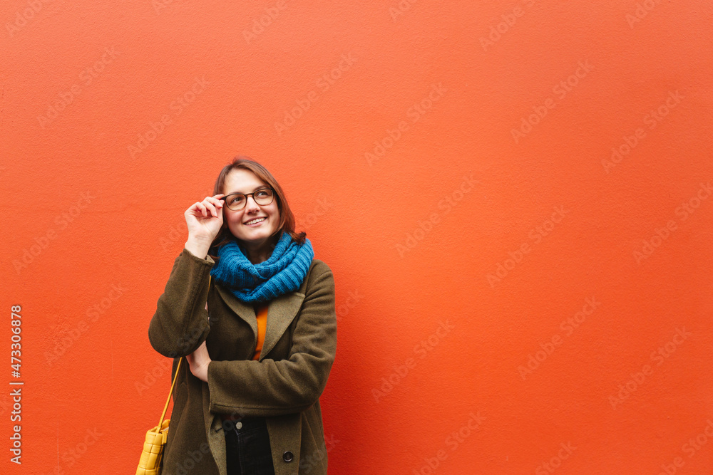Smiling woman wearing eyeglasses in front of orange wall Smiling woman wearing eyeglasses in front of orange wall