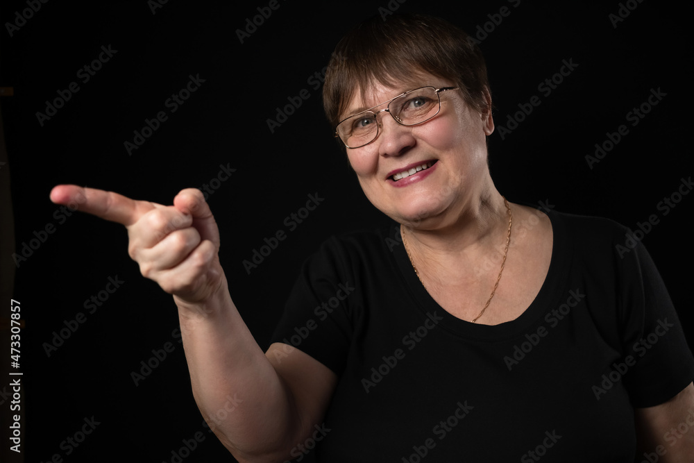 Grandmother points somewhere with her finger. Elderly woman on a black background. Grandmother points somewhere with her finger. Elderly woman on a black background.