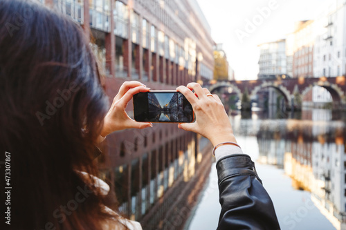 Woman photographing Ellerntorsbrucke bridge through mobile phone at canal photo