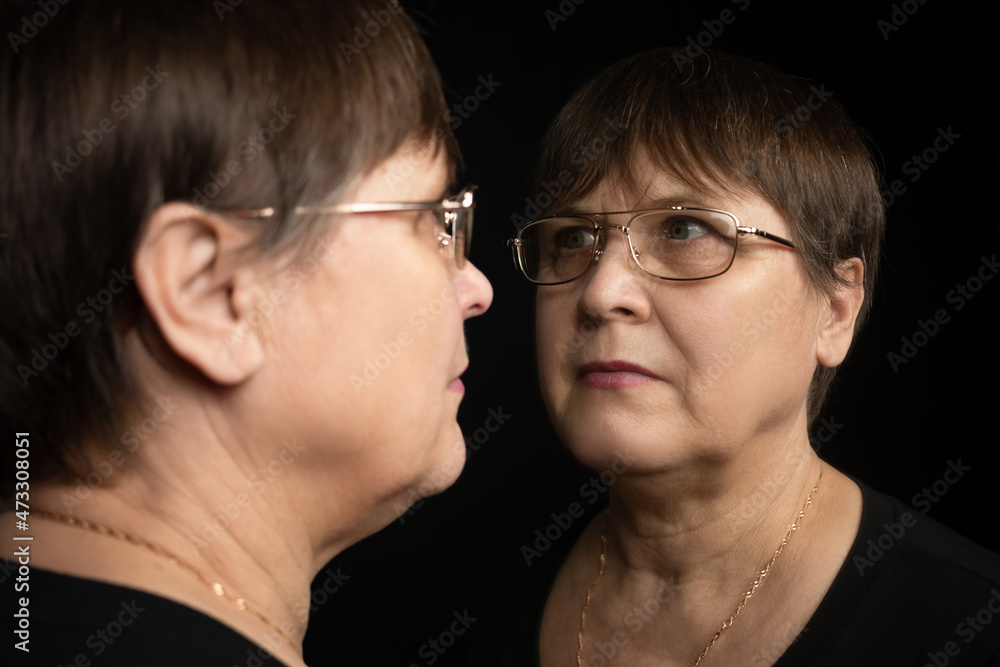 An elderly woman looks at her reflection in the mirror. An elderly woman looks at her reflection in the mirror.