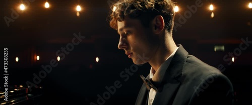 HANDHELD Young 20s aspiring musician playing grand piano on a stage of a huge concert hall. Shot with 2x anamorphic lens