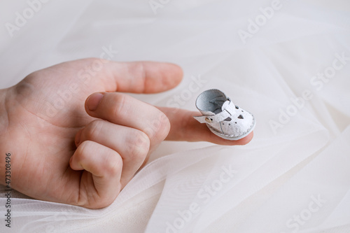 White miniature shoes for a doll made of genuine leather stand on the fingers. Beautiful shoes with a picture of a heart. Horizontal photo of clothing items.