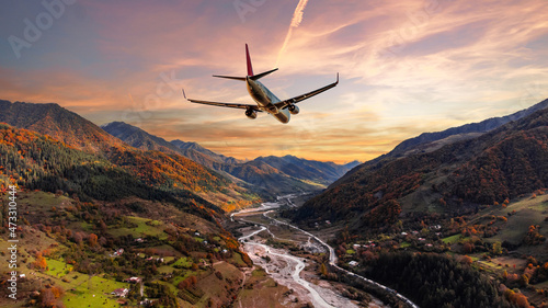 Airplane flying over scenic mountain peaks at beautiful pink sunset