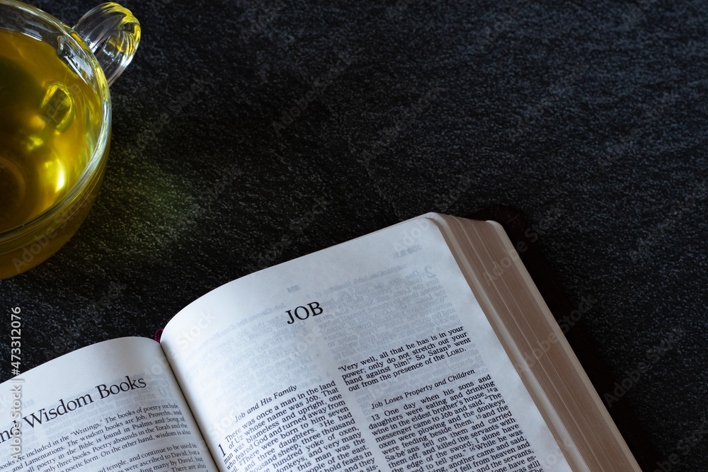 Open Holy Bible Book with a cozy cup of tea on black granite background