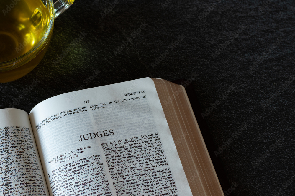 Open Holy Bible Book Judges Scripture with a hot cup of yellow tea on a