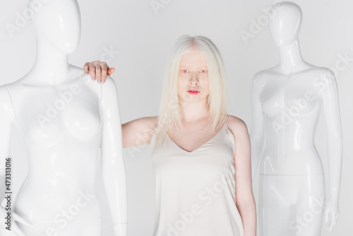 Pretty blonde and albino woman standing near mannequins isolated on white.