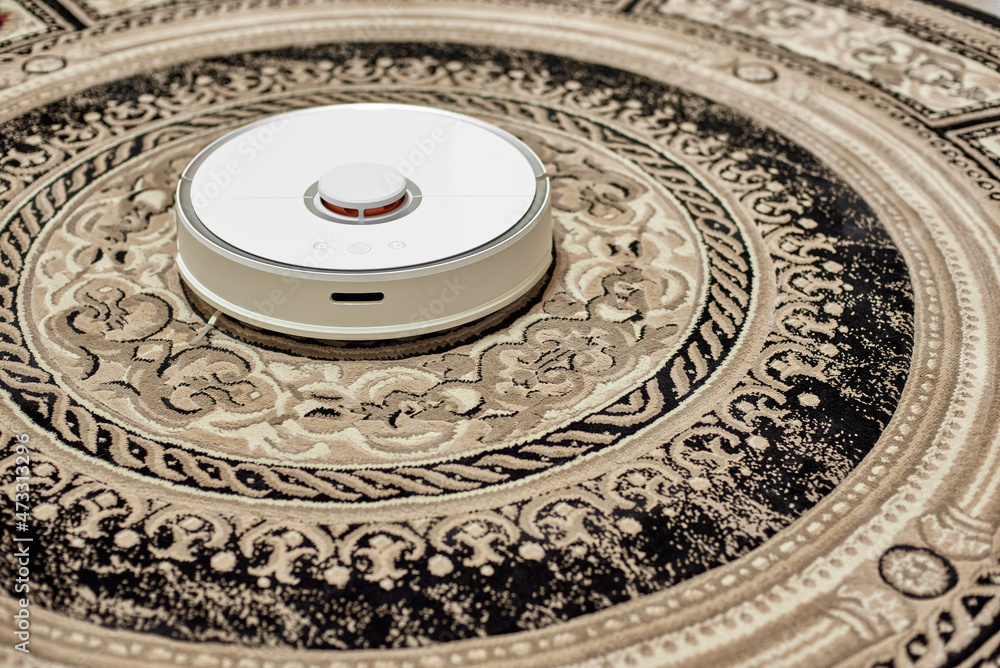 White robot vacuum cleaner isolated on a beige carpet. Side view.