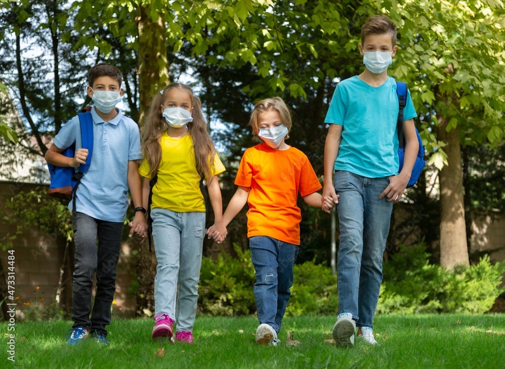 Group of schoolchildren in masks walking together on the park