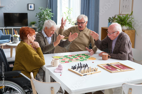 Senior man winning in the board game while sitting at the table and playing with his friends photo