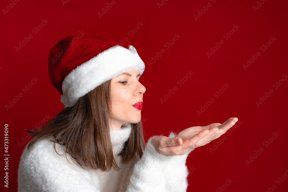 Woman in a white warm sweater and a red Santa's hat blows snowflakes off her hands Woman in a white warm sweater and a red Santa's hat blows snowflakes off her hands