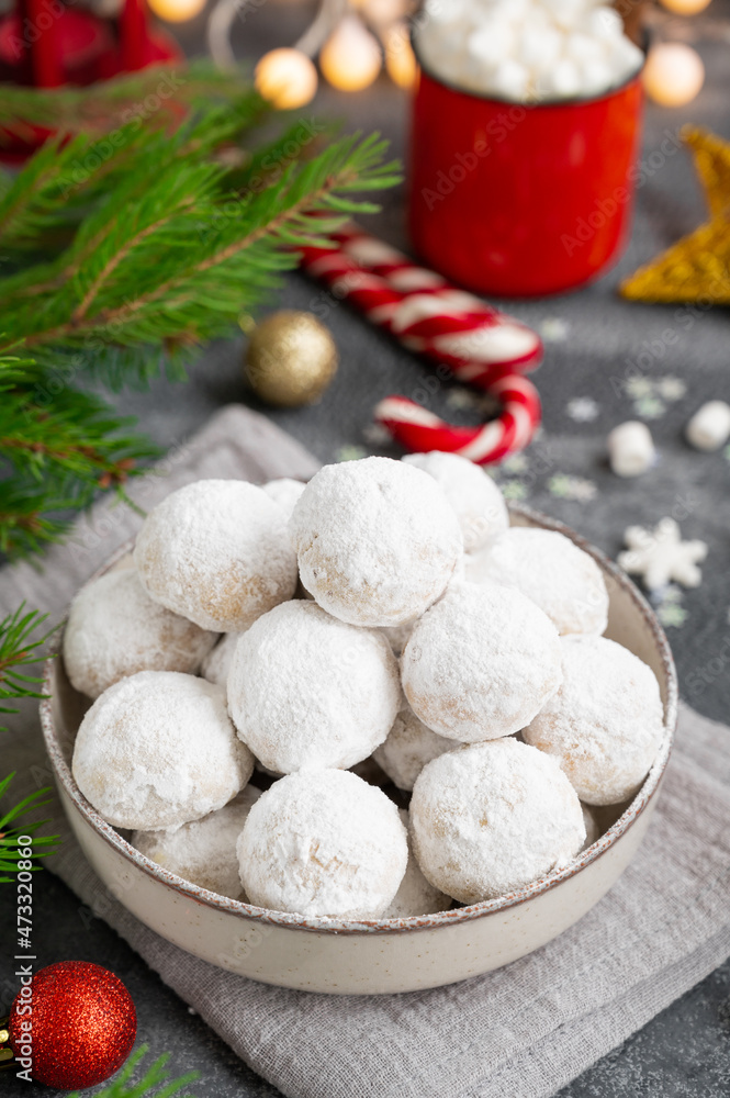 Fototapeta premium Christmas snowball cookies with walnuts and powdered sugar in a bowl on a gray concrete background with a cup of cocoa. Copy space.