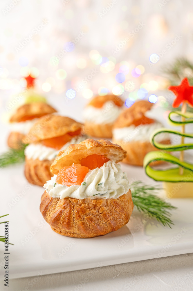Festive savory profiteroles with salmon, cream cheese and dill on a white plate on a white background. Appetizer for Christmas and New Year. Selective focus. Festive savory profiteroles with salmon, cream cheese and dill on a white plate on a white background. Appetizer for Christmas and New Year. Selective focus.