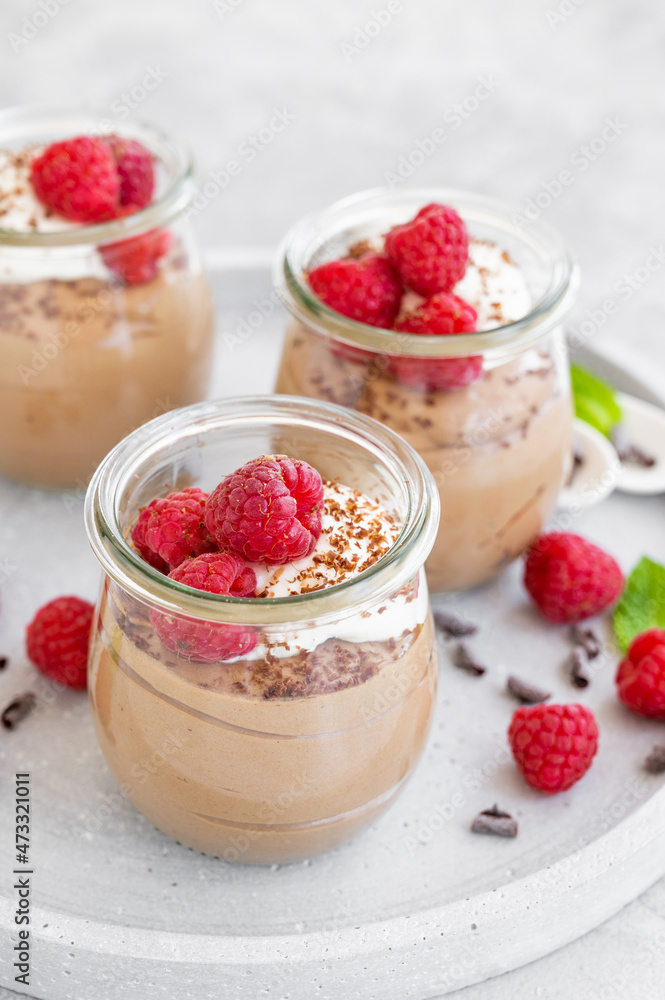 Chocolate mousse with whipped cream and fresh raspberries in a glass on a gray concrete background. Copy space. Chocolate mousse with whipped cream and fresh raspberries in a glass on a gray concrete background. Copy space.