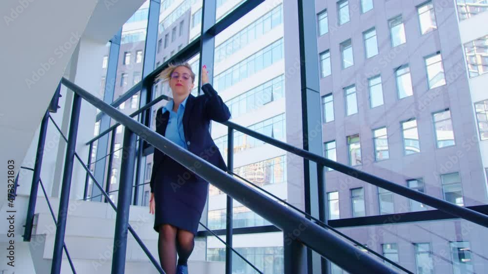 Girl in formal outfit goes down stairs inside office building in good mood dancing. Manager, employee coming back from party at work. Young woman rejoices at good news, upcoming vacation Girl in formal outfit goes down stairs inside office building in good mood dancing. Manager, employee coming back from party at work. Young woman rejoices at good news, upcoming vacation