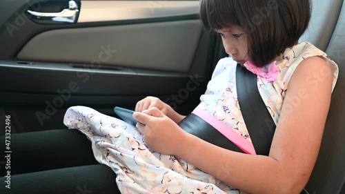little girl playing games,surfing net on the phone while traveling by car and being bored with the ride. Child is fastened with seat belt. Internet or online game addict