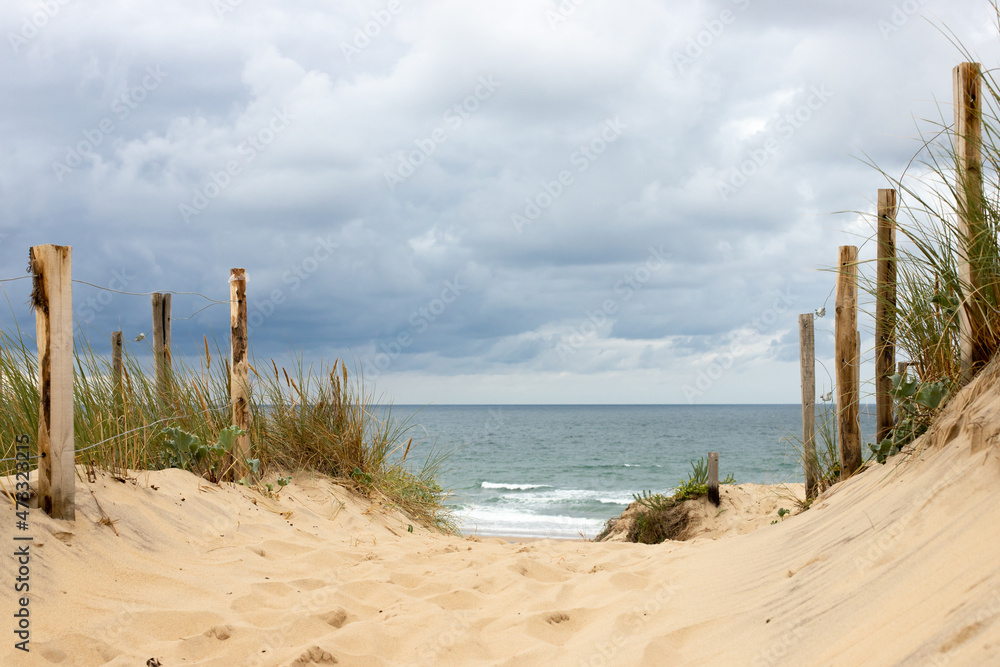 Path leading through the dunes of Soulac-sur-Mer in Médoc, France to the beach and the Atlantic Ocean with a cloudy sky in summer on vacation Path leading through the dunes of Soulac-sur-Mer in Médoc, France to the beach and the Atlantic Ocean with a cloudy sky in summer on vacation