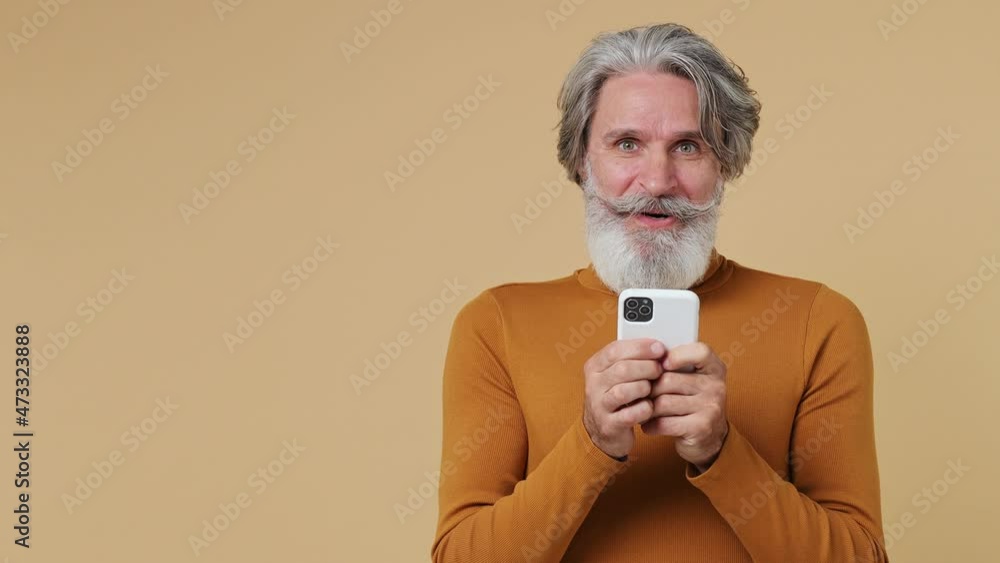 Promoter elderly gray-haired bearded man 55 years old wears shirt hold use mobile cell phone look aside on workspace copy space mockup promo area isolated plain pastel beige background studio portrait Promoter elderly gray-haired bearded man 55 years old wears shirt hold use mobile cell phone look aside on workspace copy space mockup promo area isolated plain pastel beige background studio portrait