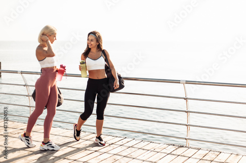 Two athletic female friends go to workout early in morning on beach