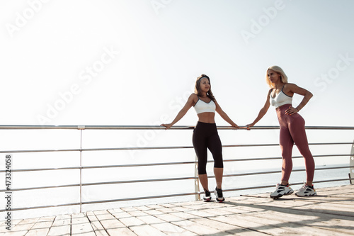 Fototapeta Naklejka Na Ścianę i Meble -  Two athletic women friend resting after intense workout on the beach
