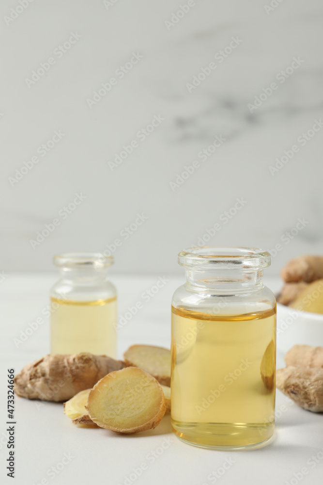 Glass bottle of essential oil and ginger root on white table Glass bottle of essential oil and ginger root on white table
