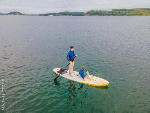 Mother and son paddling on stand up board having fun during summer beach vacation