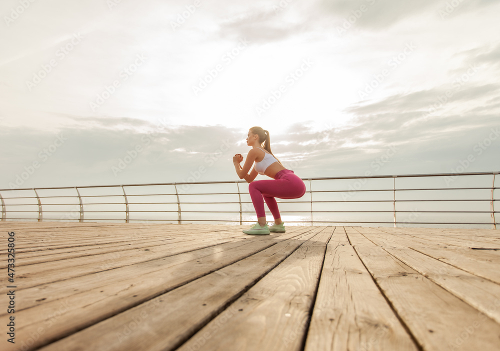 Fit woman in sportswear practicing deep squats on the beach early morning
