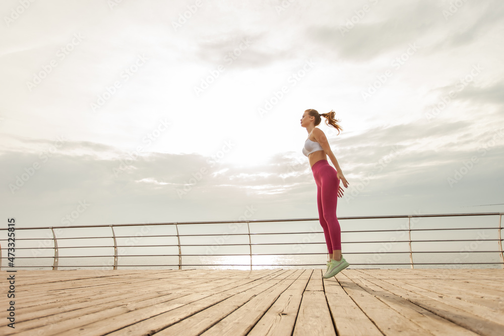 Young fit woman in sportswear is practicing jumping up on the beach early morning Young fit woman in sportswear is practicing jumping up on the beach early morning