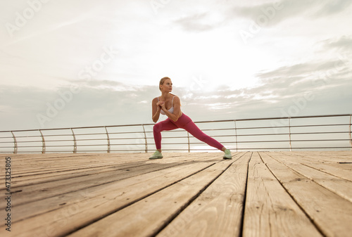 Young woman doing fitness, aerobics workout on the beach in the early morning