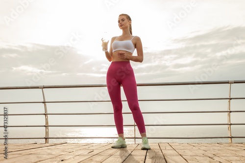Beautiful fitness model in sportswear with water bottle on the beach