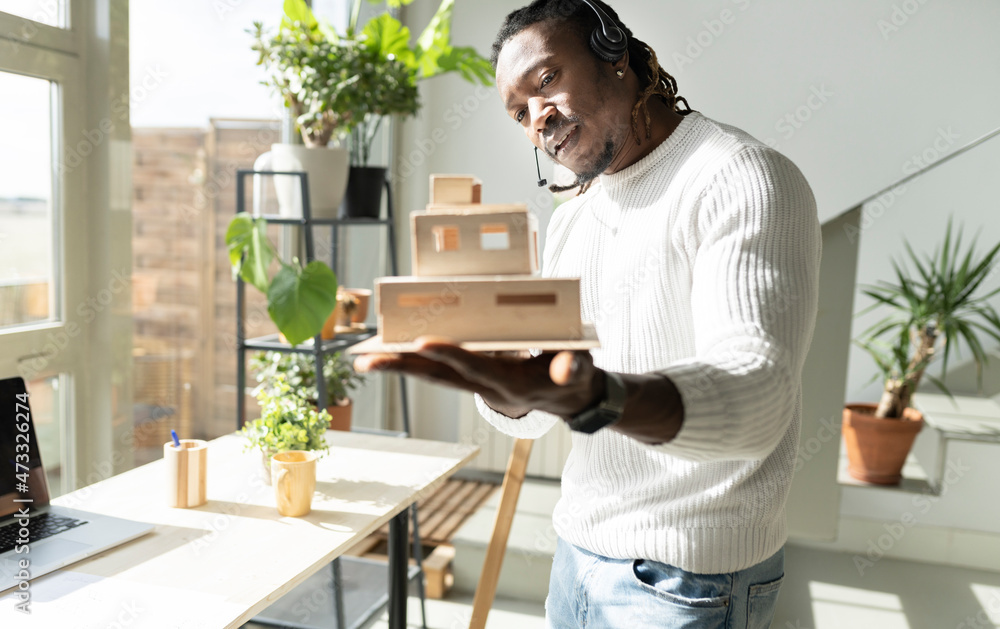 Architect wearing headset showing model on video conference through laptop in living room Architect wearing headset showing model on video conference through laptop in living room