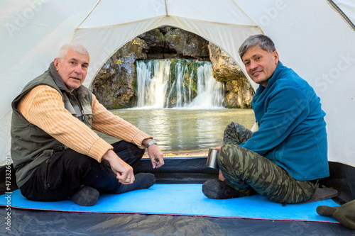 Mature male tourists sit in a tent and admire the beautiful Atysh waterfall on a sunny autumn day. Bashkortostan photo