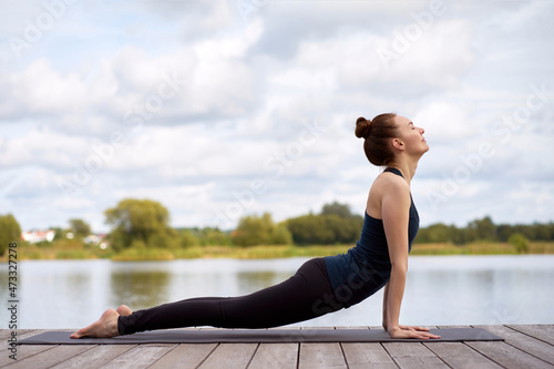Portrait of fit sporty young woman practicing yoga on yoga mat on the wooden pier near lake. photo
