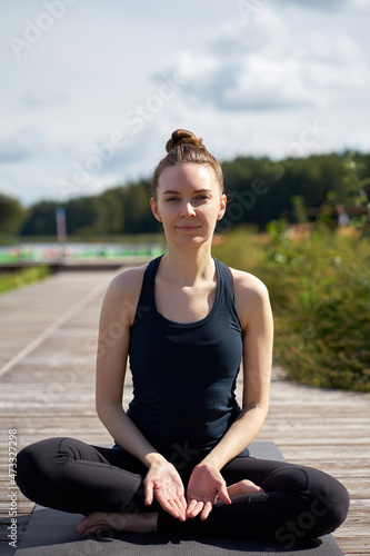 Young relaxing smiling woman practicing yoga on the wooden pier near lake. © Kiryl Lis