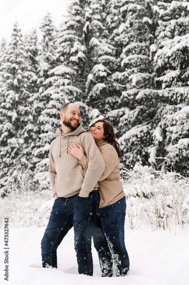 Walk in winter. Embracing couple enjoying snowfall. Man and woman having fun in the frosty forest. Romantic date in winter time.Christmas mood of a young family. Love and leisure concept Walk in winter. Embracing couple enjoying snowfall. Man and woman having fun in the frosty forest. Romantic date in winter time.Christmas mood of a young family. Love and leisure concept