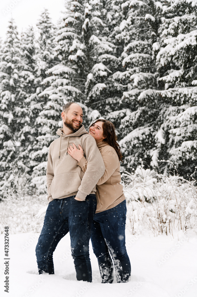 Walk in winter. Embracing couple enjoying snowfall. Man and woman having fun in the frosty forest. Romantic date in winter time.Christmas mood of a young family. Love and leisure concept Walk in winter. Embracing couple enjoying snowfall. Man and woman having fun in the frosty forest. Romantic date in winter time.Christmas mood of a young family. Love and leisure concept