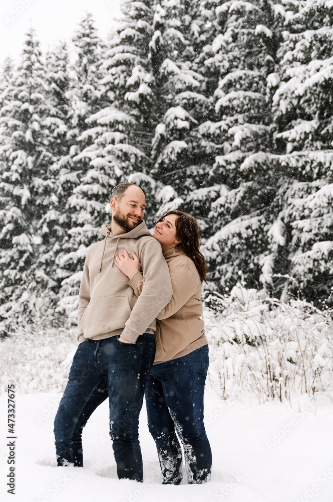 Walk in winter. Embracing couple enjoying snowfall. Man and woman having fun in the frosty forest. Romantic date in winter time.Christmas mood of a young family. Love and leisure concept Walk in winter. Embracing couple enjoying snowfall. Man and woman having fun in the frosty forest. Romantic date in winter time.Christmas mood of a young family. Love and leisure concept
