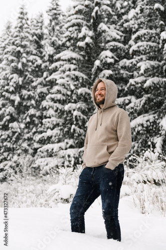 Handsome man with beard walks in a snowfall. Young man standing in the winter forest.Outdoor portrait of man posing in wood © Vadym