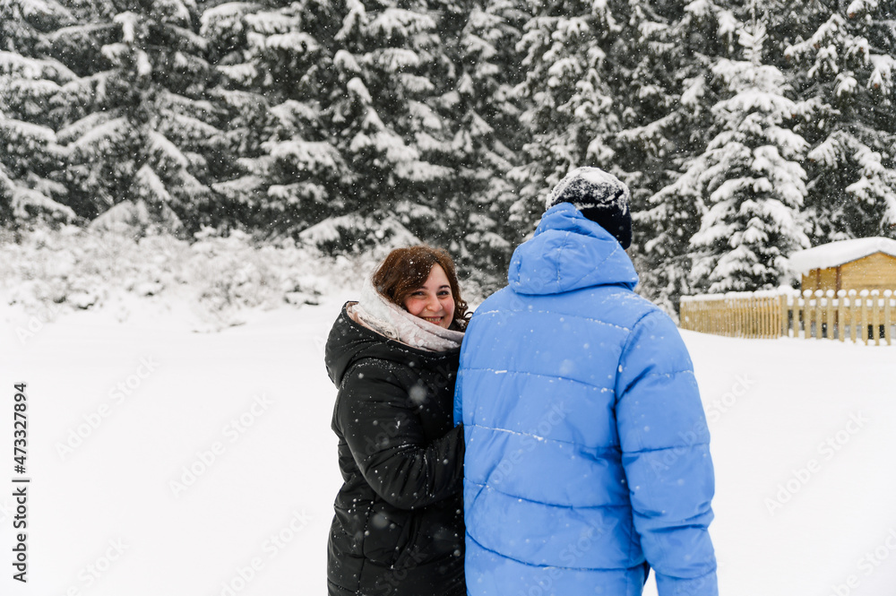 Walk in winter. Embracing couple enjoying snowfall. Man and woman having fun in the frosty forest. Romantic date in winter time.Christmas mood of a young family.  Love and leisure concept