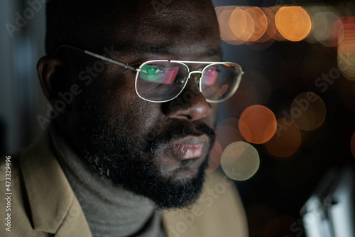 Young African businessman in eyeglasses concentrating on network while working late at night in office photo