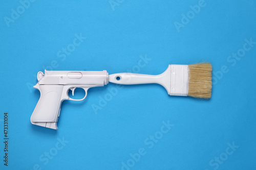White gun with paint brush on blue background. Minimal, creative layout, top view
