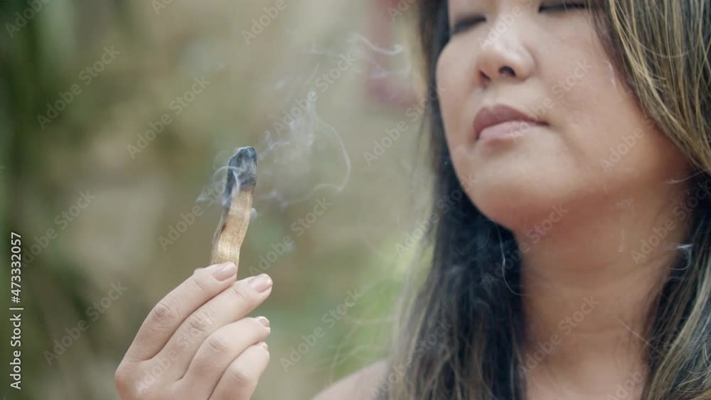Close-up shot of Japanese woman inhaling scent of fragrance. Beautiful and carefree young woman meditating outdoor, enjoying peaceful atmosphere in backyard. Aromatherapy, yoga concept Close-up shot of Japanese woman inhaling scent of fragrance. Beautiful and carefree young woman meditating outdoor, enjoying peaceful atmosphere in backyard. Aromatherapy, yoga concept