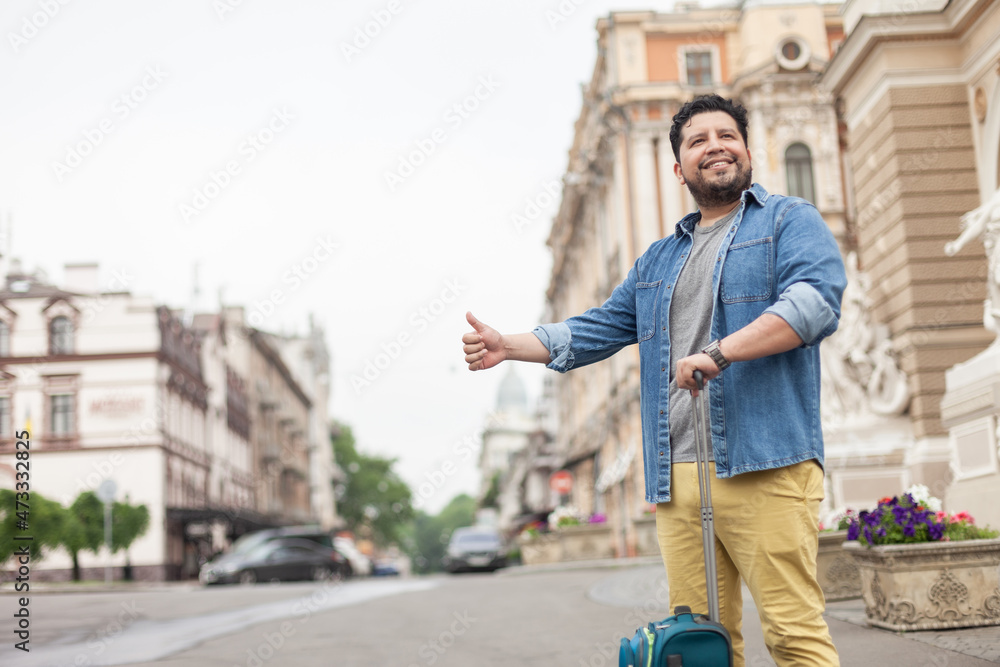 Hispanic man tourist with travel luggage catch ride in the city. Travel concept. Hitchhiking