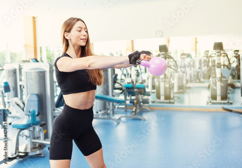 Attractive caucasian fitness woman exercising with heavy kettlebell in modern light gym. Free weight training