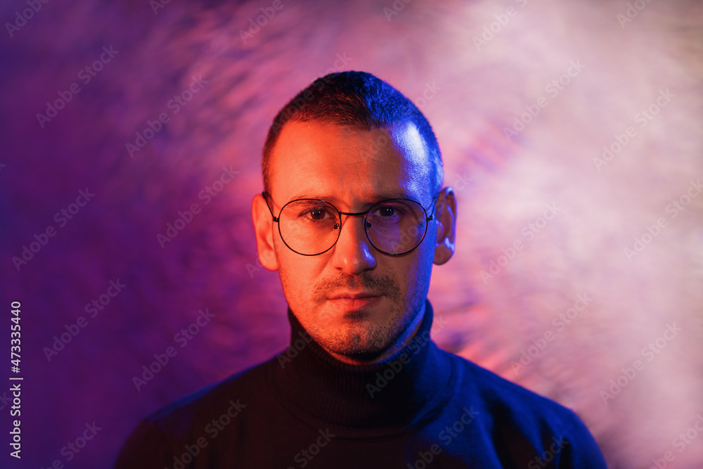 Fototapeta premium Neon portrait of serious man wearing glasses with black frame and dark turtleneck sweater on cosmic silver multicolored background